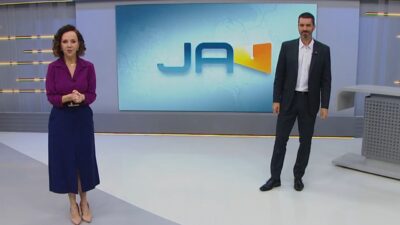 Laine Valgas e Raphael Faraco no estúdio do Jornal do Almoço diante de telão com logotipo do telejornal