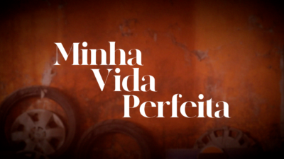 Logotipo da novela Minha Vida Perfeita em letras brancas sobre fundo alaranjado com rodas de carro desfocadas ao fundo sugerindo incêndio ou destruição