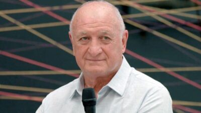 Luiz Felipe Scolari segura microfone e observa o público durante participação em programa de televisão com painel geométrico ao fundo