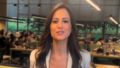 Marcela Rahal fala para a câmera em escritório da revista Veja com equipe trabalhando ao fundo durante gravação do Veja em Foco