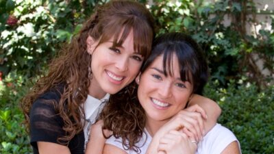 Maria José (Jacqueline Bracamontes) abraça Paula (Wendy González) em foto da novela Sortilégio diante de jardim verde