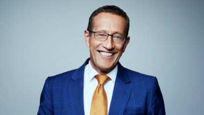 Richard Quest sorrindo de terno azul e gravata dourada em foto promocional da CNN