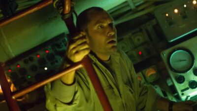 Jude Law como Robinson segura uma escada e observa com tensão o interior iluminado da sala de controle de um submarino em Mar Negro