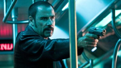 John Travolta como Ryder aponta arma dentro de vagão em cena do filme O Sequestro do Metrô 1 2 3