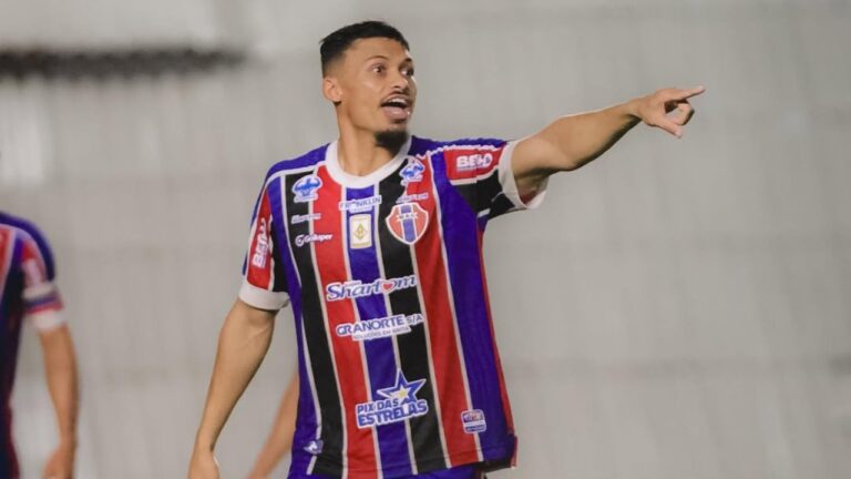 Tibúrcio aponta para o lado durante partida com camisa listrada azul vermelha e preta