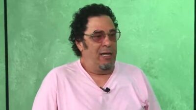 Walter Casagrande de camiseta rosa e óculos escuros durante entrevista em programa de televisão