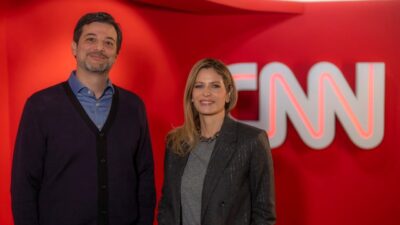 Zizo Papa e Didi Wagner posam nos bastidores da CNN Brasil diante de painel vermelho com logotipo da emissora