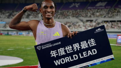 Alison dos Santos sorri e flexiona o braço ao segurar placa da Diamond League em pista de atletismo lotada