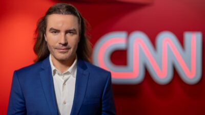 Álvaro Machado Dias posa de terno azul diante do logotipo da CNN em imagem promocional da emissora de notícias
