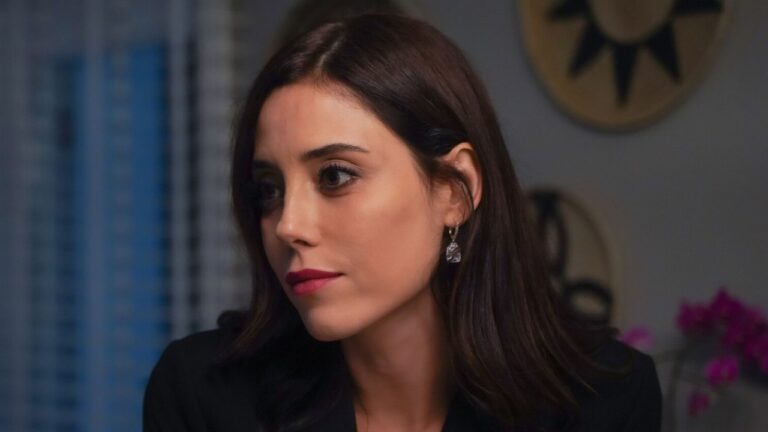 Asya Yilmaz (Cansu Dere) de blazer preto observa alguém com expressão séria em ambiente interno na novela Iludida