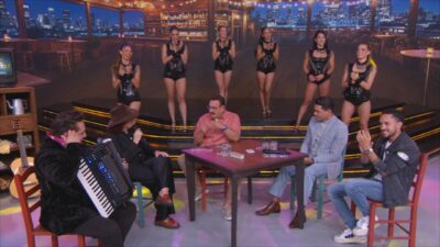 Fátima Leão conversa com Ratinho à mesa enquanto Felipe Araújo e Grelo participam do Boteco do Ratinho com bailarinas ao fundo no palco do programa