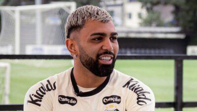 Gabigol de uniforme de treino do Santos sorri durante entrevista em campo de futebol com traves ao fundo