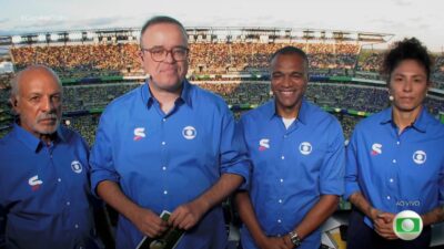 Junior, Everaldo Marques, Denilson e Cristiane de camisas azuis diante da arquibancada durante transmissão da Copa na Globo