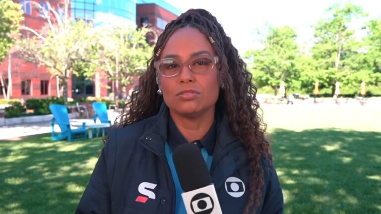 Karine Alves com microfone da TV Globo durante entrada ao vivo em área externa com árvores e edifícios ao fundo