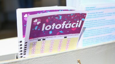 Volantes da Lotofácil organizados em expositor com cartelas de aposta e instruções de preenchimento ao fundo