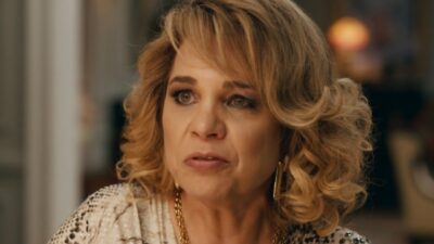 Pilar (Isabel Teixeira) com expressão apreensiva durante conversa em cena da novela Quem Ama Cuida usando colares e brincos dourados
