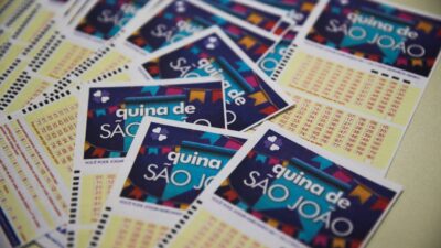 Volantes da Quina de São João espalhados sobre superfície com cartelas de apostas e dezenas impressas visíveis