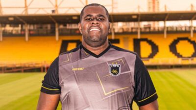 Saulo Pêgas posa com camisa do Volta Redonda no gramado do estádio diante das arquibancadas amarelas