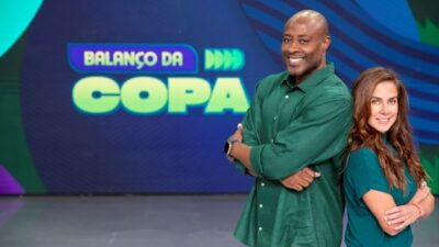 Wallace Neguerê e Carol Barcellos posam de braços cruzados no estúdio do Balanço da Copa diante do telão do programa no SBT