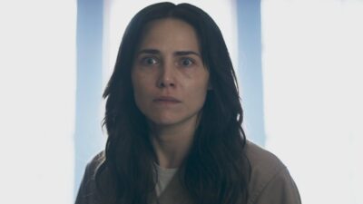 Adriana (Leticia Colin) de olhos arregalados encara à frente diante de janelas desfocadas em cena de Quem Ama Cuida