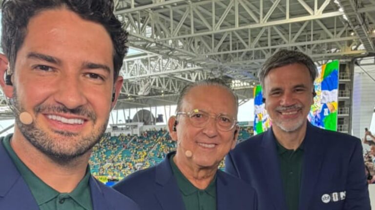 Alexandre Pato, Galvão Bueno e Mauro Beting sorriem com microfones de transmissão em cabine de estádio de futebol