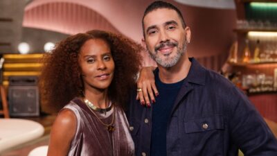 Aline Wirley e André Marques sorriem lado a lado em estúdio com cenário de programa ao fundo