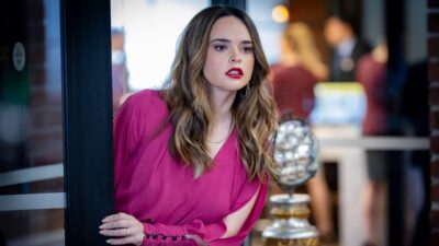 Camila Montes (Fabiola Guajardo) de vestido rosa espreita atrás de uma porta com expressão tensa em ambiente interno da novela A História de Joana, a Virgem
