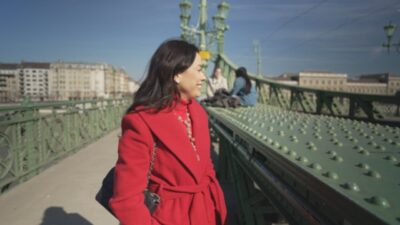 Daniela Filomeno de casaco vermelho sorri sobre ponte metálica durante gravação do CNN Viagem & Gastronomia