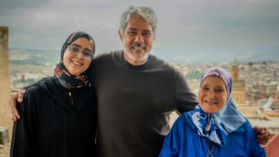 Fatima Sakout, William Bonner e Fatima Haja Amrani sorriem abraçados diante de vista panorâmica da cidade usando roupas casuais e véus islâmicos