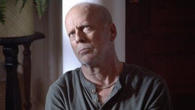 Frank (Bruce Willis) de camisa cinza e expressão séria, olhando para cima em cena de Sobreviver à Noite