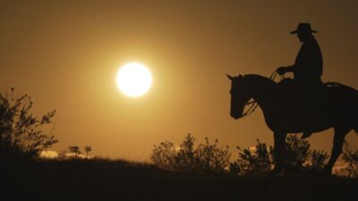 Cavaleiro de chapéu conduz cavalo em silhueta ao pôr do sol no Pampa em reportagem do Globo Repórter