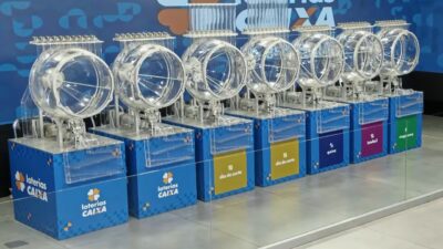 Globos transparentes dos sorteios das Loterias Caixa alinhados em estúdio com máquinas da Mega-Sena, Quina, Lotofácil e Dia de Sorte