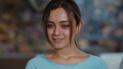 Gulru Celik (Damla Sonmez) sorri com blusa azul-clara e cabelo preso em cena da novela Guerra das Rosas