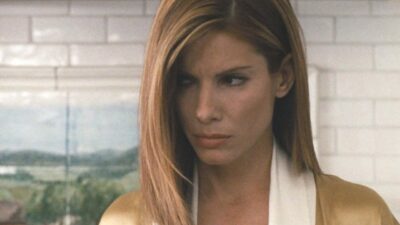 Jean (Sandra Bullock) com expressão tensa e olhar para baixo diante de parede branca em cena de Crash: No Limite