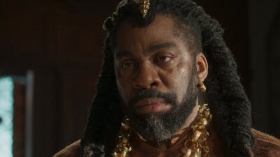 Jendal (Lázaro Ramos) com tranças, barba e colares dourados encara alguém em cena da novela A Nobreza do Amor