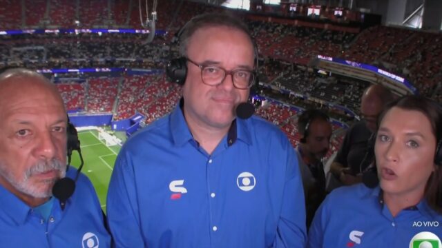 Junior, Everaldo Marques e Ana Thaís Matos de headset na cabine de transmissão com estádio e gramado ao fundo durante a Copa