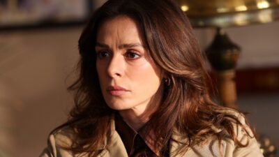 Karsu (Ozge Ozpirincci) com expressão séria usa casaco bege em ambiente interno na novela Coração de Mãe