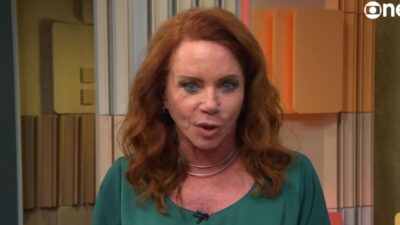 Leilane Neubarth de blusa verde fala em estúdio da GloboNews com painéis ao fundo