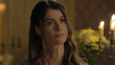 Lívia (Alinne Moraes) com expressão séria e olhar fixo em ambiente iluminado por velas em cena de Além do Tempo