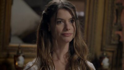 Lívia (Alinne Moraes) de cabelos longos olha à frente em ambiente com quadros, em cena de Além do Tempo