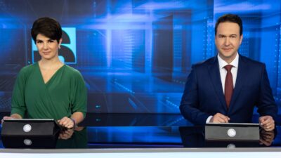 Mariana Godoy e Eduardo Ribeiro na bancada do Jornal da Record com tablets e telão azul ao fundo