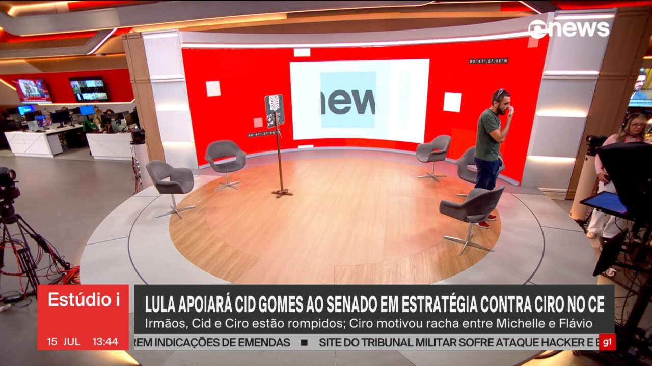 Novo estúdio da GloboNews com telão vermelho, cadeiras para entrevistas e equipe prepara gravação na redação