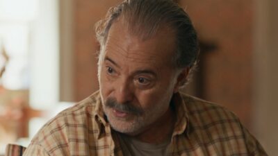 Otoniel (Tony Ramos) de camisa xadrez com expressão séria em ambiente interno na novela Quem Ama Cuida