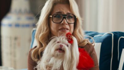 Pilar (Isabel Teixeira) com expressão apreensiva segura cachorro branco no sofá em cena de Quem Ama Cuida