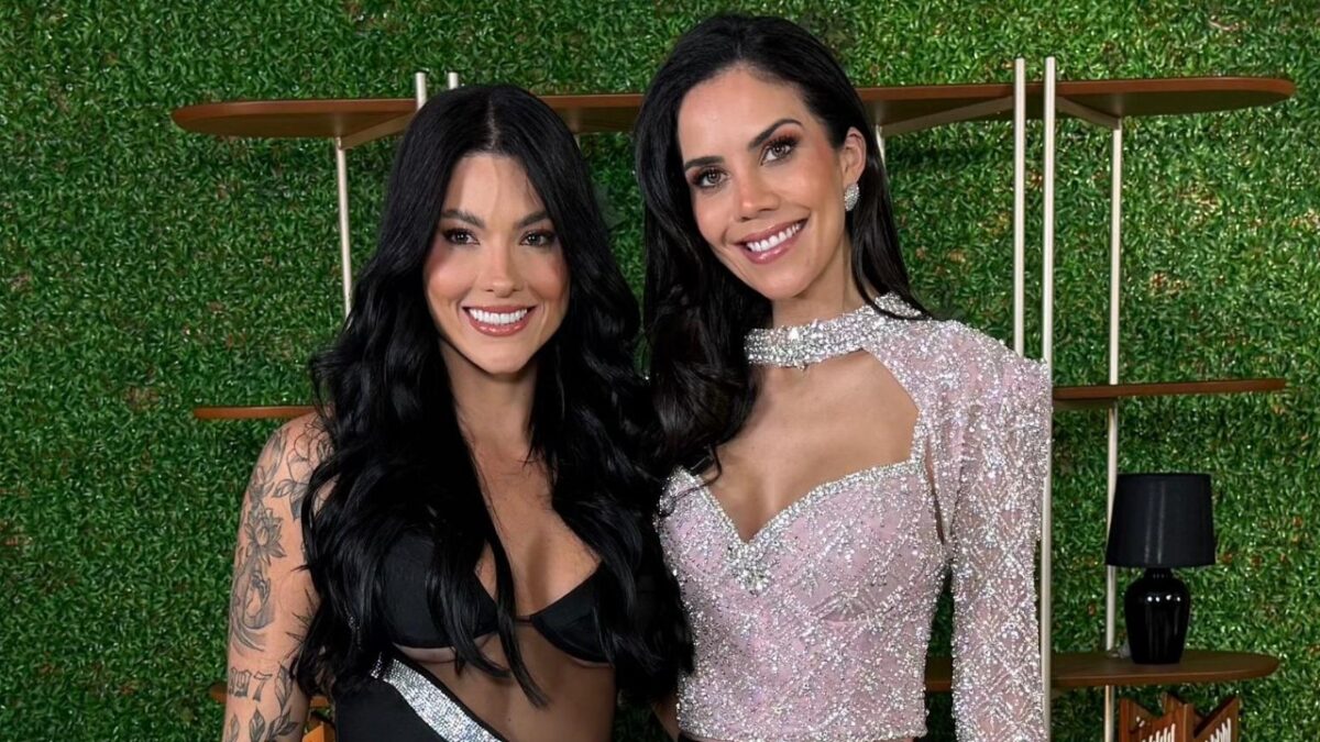 Rayane Figliuzzi e Daniela Albuquerque sorriem lado a lado usando vestidos de festa diante de parede verde decorativa