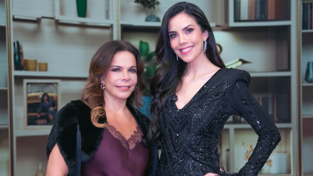 Sula Miranda e Daniela Albuquerque sorriem lado a lado, de vestidos escuros, em ambiente interno com estante ao fundo