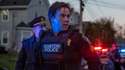 Tommy Saunders (Mark Wahlberg) veste colete da Polícia de Boston e olha para o lado durante operação policial noturna com viaturas e outro policial ao fundo