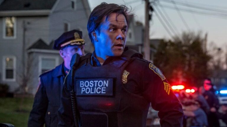 Tommy Saunders (Mark Wahlberg) veste colete da Polícia de Boston e olha para o lado durante operação policial noturna com viaturas e outro policial ao fundo