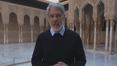 William Bonner de suéter preto fala em pátio com arcos ornamentados durante gravação do Globo Repórter