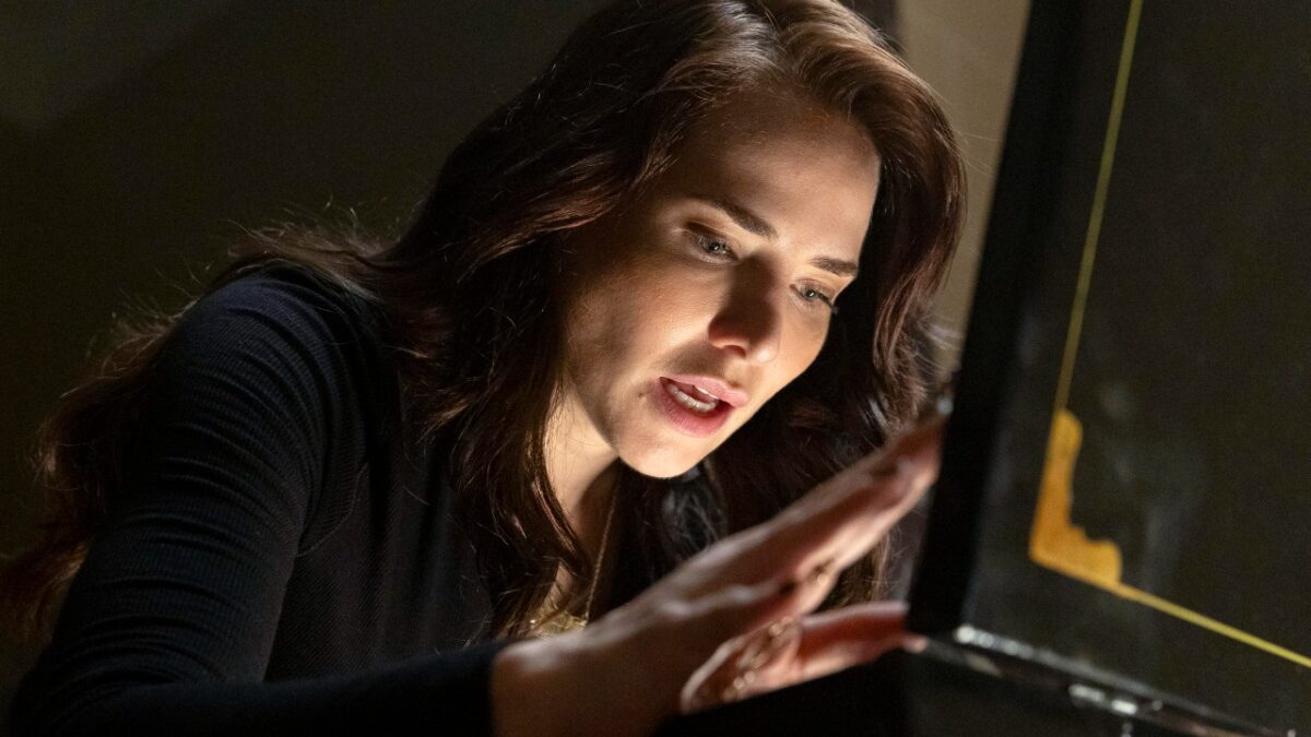 Adriana (Letícia Colin) observa e toca objeto iluminado com expressão concentrada em cena de Quem Ama Cuida